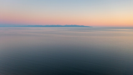 Sunset seascape. Aerial view of the sea. Mountains in the distance. Ripples on the surface of the water. Beautiful natural background. Perfect for design.