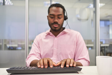 Afrikanischer Business Mann mit Headset schreibt auf Computer