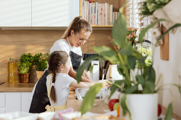 Young beautiful mother and shooler kids in the kitchen after baking cookies biscuits pie washing dishes in the sink. Standing in the beautiful kitchen talking and smiling.