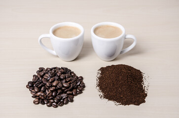 Two coffee cups or mugs with beans and ground coffee on wooden desk or table close-up coffee making concept