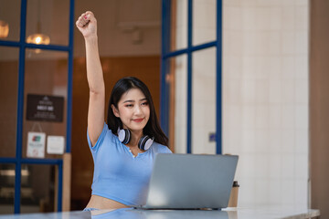 Beautiful Asian woman wearing headphones on her neck excited working in front of a laptop.