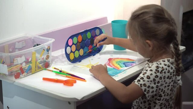 Talented Creative Child Girl Female Artist Draws Rainbow sky summer on Paper, Using Fingers Paints Brush Creates Colorful, Kid Drawing on table at Home. Painter Creating Abstract Modern Art. Childhood