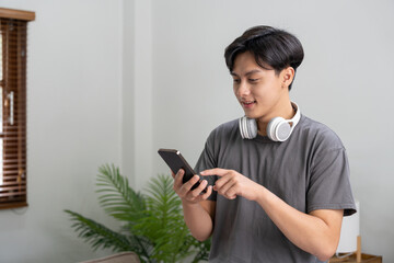 Smiling man using mobile phone and listening music through headphones at home