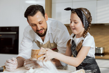 Curious daughter sieving flour on wooden surface with delighted young father. Preparing cooking...