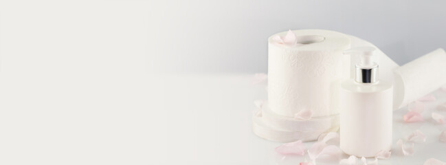Hygiene banner with roll of toilet paper with cosmetic dispenser bottle on light background with copy space. White toilet tissue. Restroom soft touch toilet paper. Soft focus style, banner size
