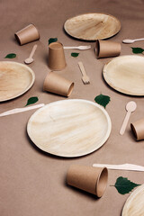 Set of different eco-friendly tableware with green birch leaves on brown paper  background. Bamboo plates, paper cups and wooden cutlery.