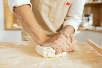 Man's hands kneading homemade dough with wheat flour close-up shot on wooden surface in modern kitchen.