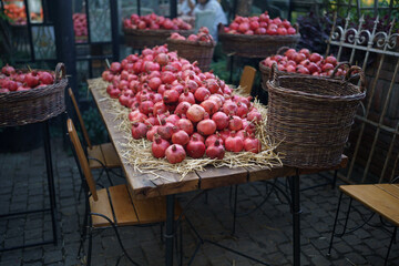 Harvest of ripe pomegranates for juice on wooden table with straw at outdoor farmers market in Tbilisi Georgia, shallow depth of field. Vegetarian healthy food