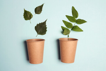 Eco-friendly coffee to go cups with green leaves on blue background.