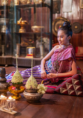 Portrait photo of a young beautiful asian Laos lady wearing traditional Lao costume dresses with flower bouquet and candles prepared for Loy Krathong festival sitting on the floor with a elegant pose