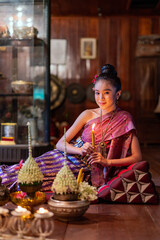 Portrait photo of a young beautiful asian Laos lady wearing traditional Lao costume dresses with flower bouquet and candles prepared for Loy Krathong festival sitting on the floor with a elegant pose