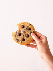 Female hand holding bitten an American chocolate chip cookie in the air in front of the white...