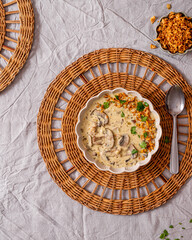 vegan creamy Mushroom soup with crispy fried onions and fresh parsley in a plate closeup top view on a grey linen table with rafia plate holders