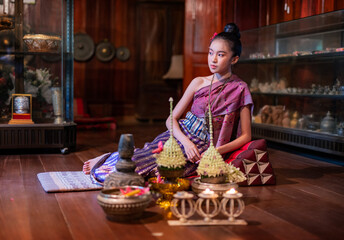 Portrait photo of a young beautiful asian Laos lady wearing traditional Lao costume dresses with flower bouquet and candles prepared for Loy Krathong festival sitting on the floor with a elegant pose