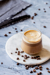 Ice-cold creamy coffee brew ion a marble round tray on a blue table with some coffee beans spread around, a close-up cold drink