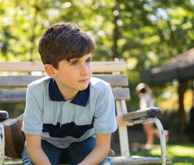 portrait of handsome caucasian teenage child boy sitting on bench in a park looking away. Beautiful sunny day