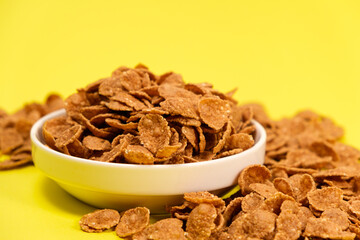 Durum wheat flakes - quick breakfast cereal on a plate on a yellow background, space for text.