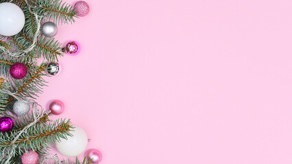 Pastel pink background with copy space and silver pine branches decorated with pink and white ornaments. Flat lay