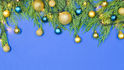 Fir garland with decorative lights and gold and blue vibrant ornaments on blue background. Copy space flat lay