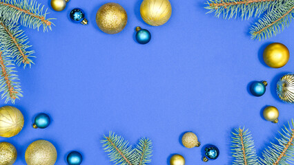 Christmas frame with vibrant blue and gold ornaments and fir branches on blue background. Glamour flat lay copy space concept