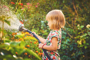 Cute little girl watering flowers with a hose in the garden
