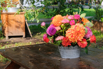 Autumn flowers: roses, asters, dahilia in the garden on a wooden table. Floristic design. Sunny day.