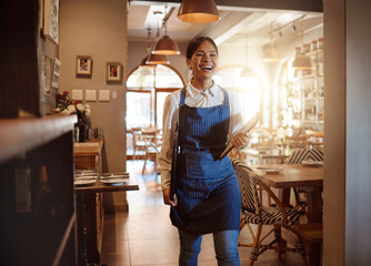 Woman, happy and waitress in restaurant working in apron with food menu in hand for table. Girl, smile and service work at luxury diner, cafe or coffee shop show happiness on face for job in London