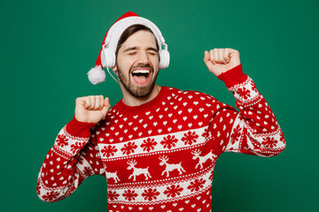 Merry joyful happy young man wear red warm knitted sweater Santa hat headphones posing listen music...