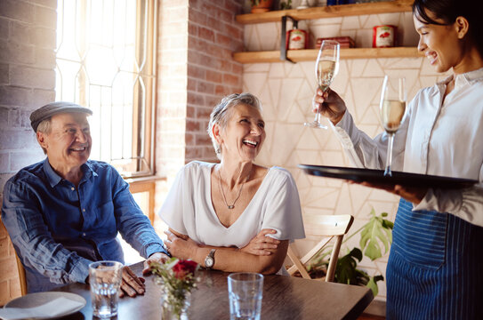 Senior couple, waiter and champagne in restaurant for wedding anniversary, celebration or birthday. Happy elderly man and woman smile with waitress and serve alcohol to celebrate retirement event