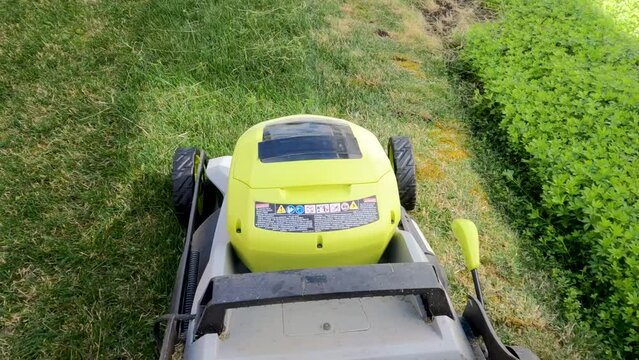 Action cam shot of an electric lawn mower quickly moving alongside a flower bed.