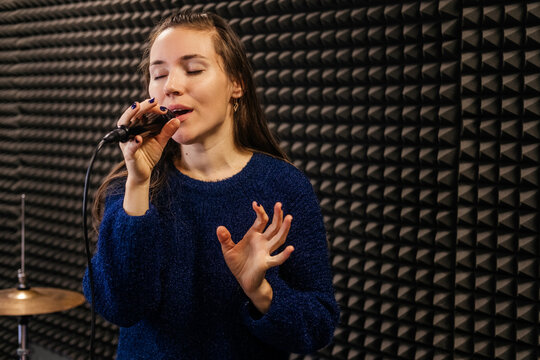Caucasian woman with microphone recording song in professional studio. Female singer indoor