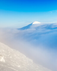 Mountaine Hoverla capped with snow on winter during snow storm at sunset. View at the peak over clouds of highest mountain of Ukraine - Hoverla from the mountaine Petros. Vertical format photo.