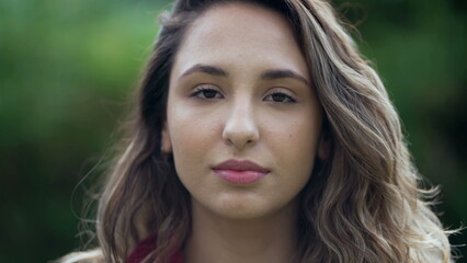 Portrait of a young hispanic woman looking at camera. Casual South American latina girl face closeup standing outdoors at park 2