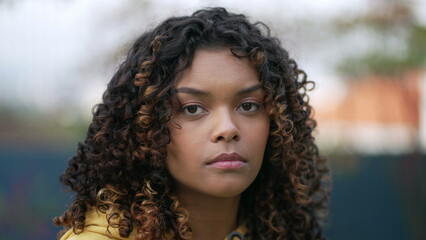 Portrait of a serious black girl standing outdoors looking at camera. Closeup female African American young woman with curly hair