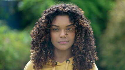 Portrait face closeup of a Brazilian black young woman with curly hair looking at camera. African American hispanic latin girl standing outdoors