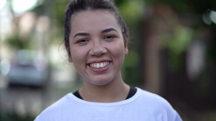 One Brazilian hispanic young woman walking forward toward camera. South American girl in 20s smiling in city street sidewalk