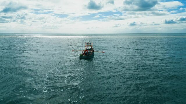 Fishing trawler, boat, ship sailing into the midday sun, trawling for fish off the Lincolnshire coast, near Skegness in the UK. showing boat pulling nets across a blue sea. Aerial, video footage