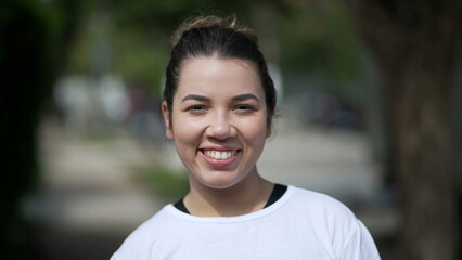 Obraz premium Happy young woman portrait face closeup standing outside looking at camera. Casual female person in 20s stands outdoors