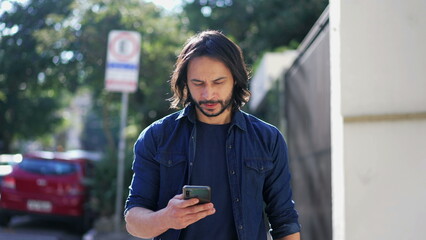 Fototapeta premium Man holding smartphone walking in urban city street. Tracking motion shot of a person checking phone going forward