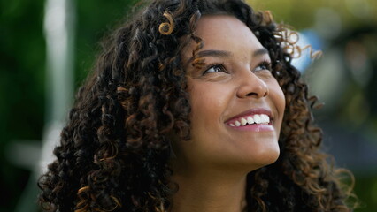 Happy African American woman closeup face looking up at sky smiling. One hopeful black hispanic 20s...