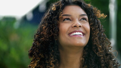 Happy African American woman closeup face looking up at sky smiling. One hopeful black hispanic 20s adult girl