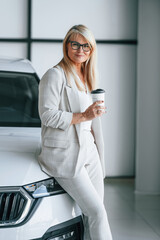 Standing and posing. Woman in white formal clothes is in the car dealership