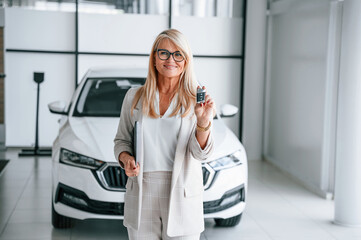 New automobile owner. Woman in white formal clothes is in the car dealership