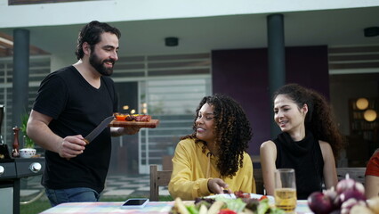 Barbecue chef serving food to friends and family at BBQ party. Happy group of diverse people celebrating holidays together