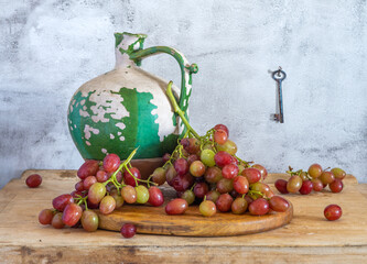 A bunch of ripe and tasty grapes and an old ceramic jug