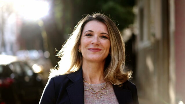 Smiling Confident Older Woman Walking Outdoors With Sun Backlight. Proud Mature Lady Walks Forward Face Closeup