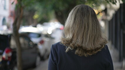 Back of person walking in city street. Contemplative woman walks outdoors in urban sidewalk