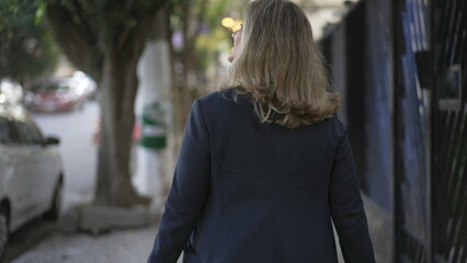Back of person walking in city street. Contemplative woman walks outdoors in urban sidewalk