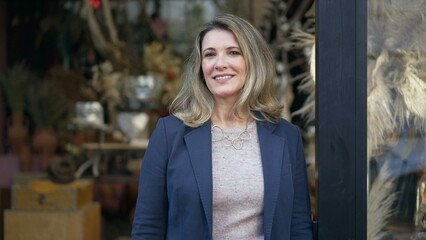 Portrait of a middle age female entrepreneur standing in front of small local business shop looking at camera