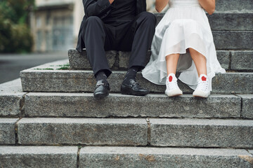 Sitting on the stairs. Beautiful bride with his fiance is celebrating wedding outdoors